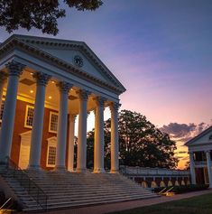 an old building with columns and pillars lit up at night, in front of trees