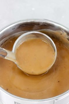 a ladle full of peanut butter sits in a silver pot on a white surface