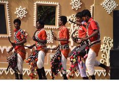 men in orange and white outfits are performing on stage with musical instruments while another man is standing behind them