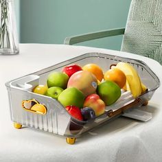 a plastic container filled with assorted fruit on top of a table next to a glass vase