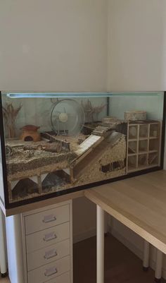 a fish tank sitting on top of a wooden table next to a white cabinet with drawers