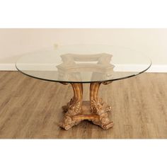 a glass top table with carved wood legs on wooden flooring in front of a white wall