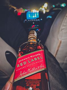 a bottle of red label sitting in the back seat of a car with someone holding it