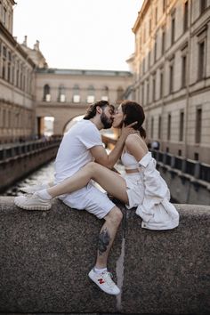 a man and woman sitting on the edge of a bridge kissing