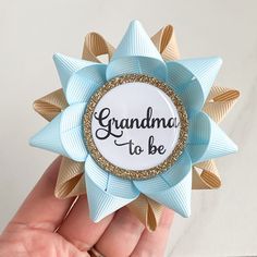 a hand holding a blue and gold brooch with the words grandma to be on it