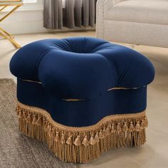 a blue velvet ottoman with tassels and fringe trim around the edges, in a living room