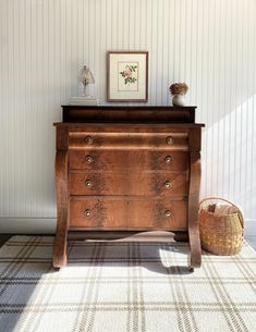 a wooden dresser sitting next to a basket on top of a rug in a room