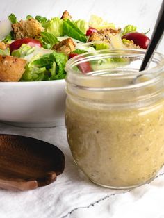 a salad with dressing in a jar next to a wooden spoon on a white tablecloth