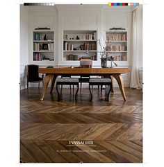 a dining room table with chairs and bookshelves in the back ground, on top of wooden parquet flooring