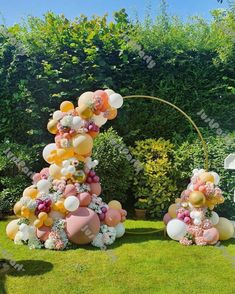 an outdoor decoration with balloons and flowers in the shape of trees on green grass, surrounded by shrubbery