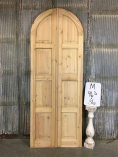 a tall wooden door sitting next to a white lamp on top of a cement floor