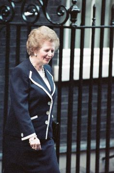 an older woman walking down the street in front of a black iron fence and gate