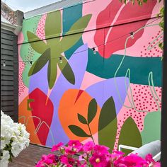 a colorful mural on the side of a building with pink flowers in front of it