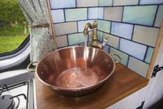 a copper bowl sink on top of a wooden counter next to a window with green grass in the background