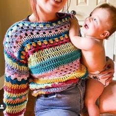 a woman holding a baby in her arms and wearing a multicolored crocheted sweater