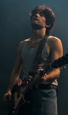 a young man holding a guitar in his right hand and looking up at the sky