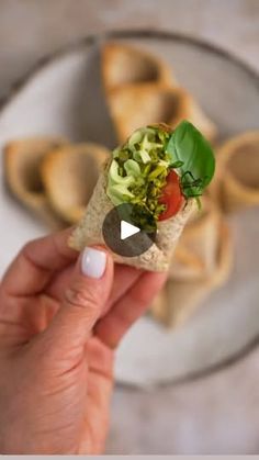 a person holding a piece of bread with veggies in it on a plate