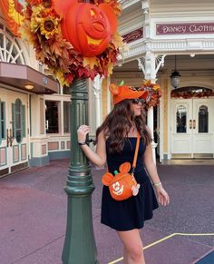 a woman in a black dress is standing next to a pole with pumpkins on it