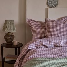 a bed with purple and green checkered comforter next to a lamp on a night stand