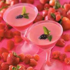 two glasses filled with liquid and garnished with berries on the table next to strawberries