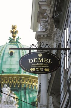 a sign hanging from the side of a building with a green dome in the background