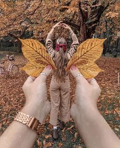 a person holding up a yellow leaf in front of a tree