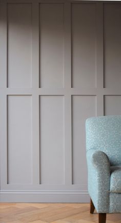 a blue chair sitting in front of a wall with white paneling on the walls