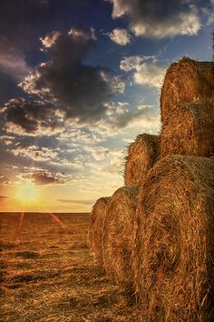 hay bales are stacked up in the field as the sun sets over the horizon