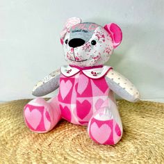 a pink and white teddy bear with hearts on it's chest sitting on a brown surface