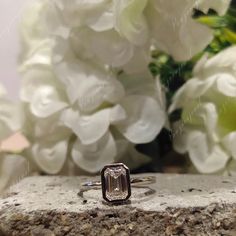 a close up of a ring on a rock with white flowers in the back ground