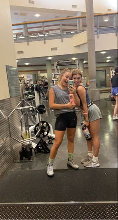 two women standing in the gym with their arms around each other and smiling at the camera