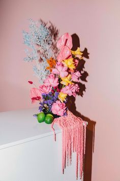 a bouquet of flowers sitting on top of a white dresser next to a pink wall