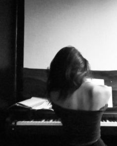 a woman sitting at a piano in front of a screen with her back turned to the camera