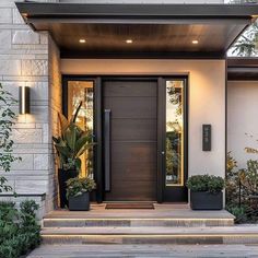 the front entrance to a modern home with potted plants on the steps and lights on