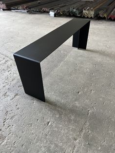 a black bench sitting on top of a cement floor next to piles of metal sheets