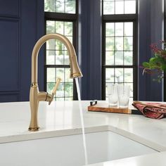 a kitchen faucet with water running from it's spout and windows in the background