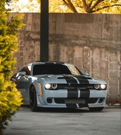 a gray and black striped car parked in front of a stone wall next to trees