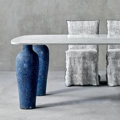 a white table with four blue vases sitting next to it on top of a cement floor