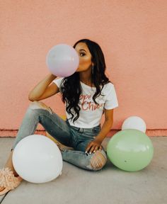 a woman sitting on the ground with balloons in front of her and one balloon blowing