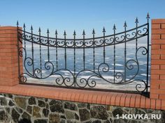 an iron fence on top of a brick wall near the ocean with waves in the background