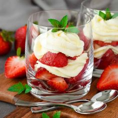 two desserts with strawberries and whipped cream in them on a wooden cutting board