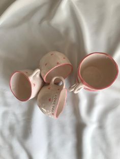 three coffee mugs sitting on top of a white bed covered in pink polka dots