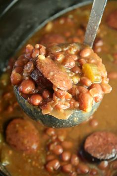 a ladle full of beans and meat in a pot with a spoon sticking out