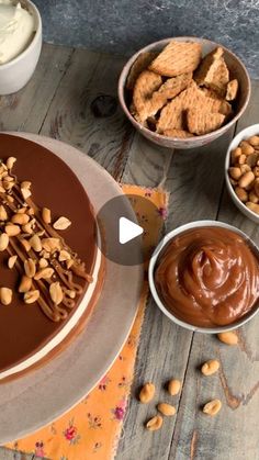 a cake with nuts and chocolate frosting in bowls next to it on a table