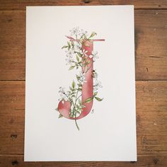 the letter j is made up of flowers and leaves on a white paper with a red ribbon