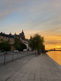 the sun is setting over the water and buildings on the other side are lined with trees