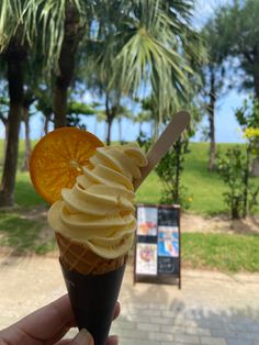 a hand holding an ice cream sundae in front of a park with palm trees