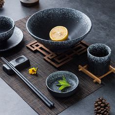 a table topped with black bowls filled with food next to chopsticks and pine cones