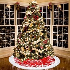 a decorated christmas tree in front of two large windows with holiday decorations on the top