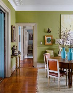 a dining room with green walls and wooden flooring is pictured in this image, there are two vases on the table